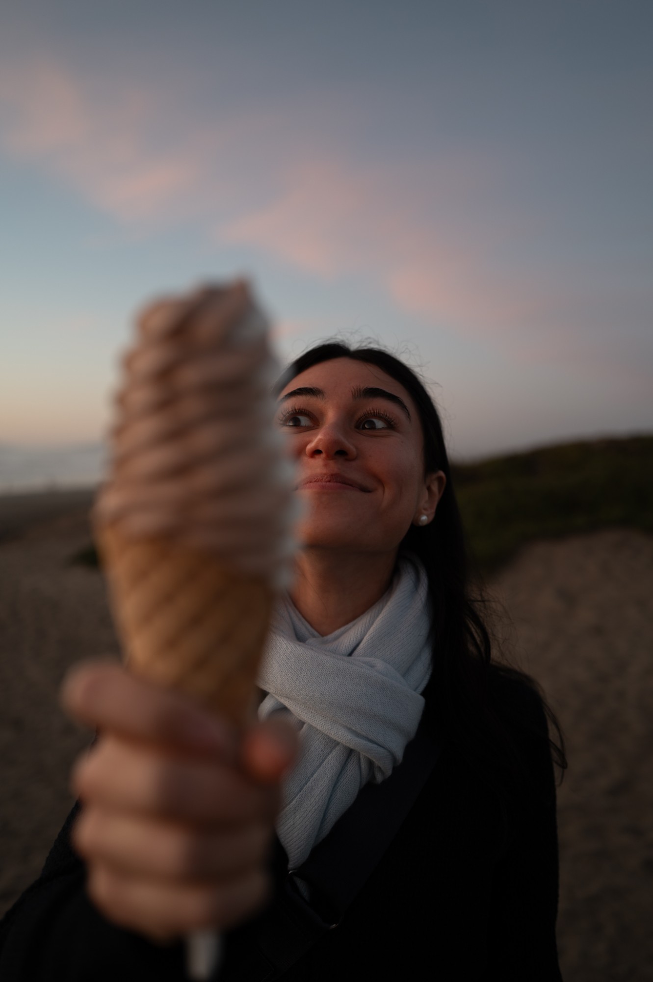 Holding a soft-serve cone up to the camera at the beach at dusk